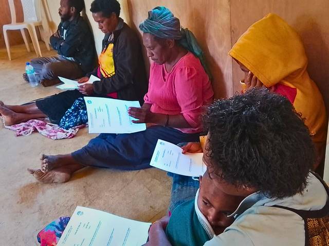 Women seated on a floor read printed handouts during a session.